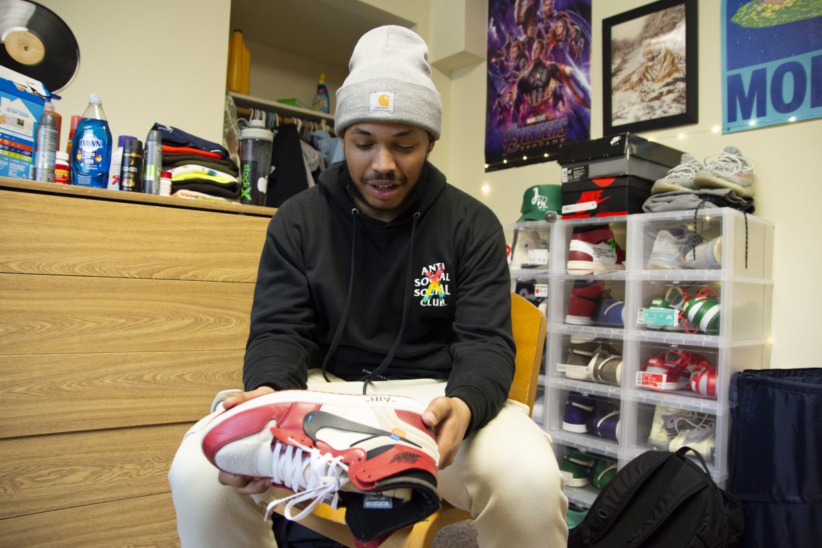 Sophomore Bronson Pea shows off his favorite pair of sneakers in his dorm room. Behind him is the shelving unit used to house the rest of his valuable shoe collection. | Photo by Emma Gottschalk