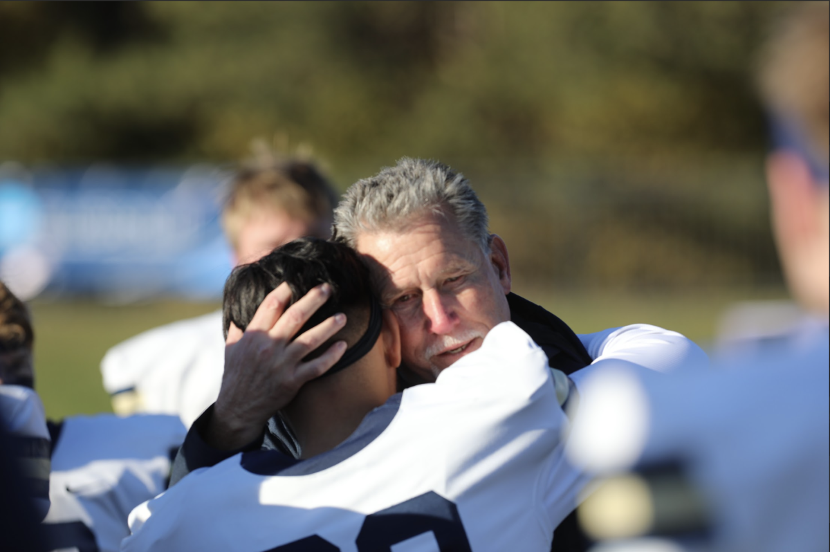 Bethel University Head Football Coach Steve Johnson says goodbye to junior kicker Hugo Cifuentes after the last game of his coaching career. After the Royals’ loss, the team huddled around its coach, exchanging hugs with Johnson and each other, many of them crying.