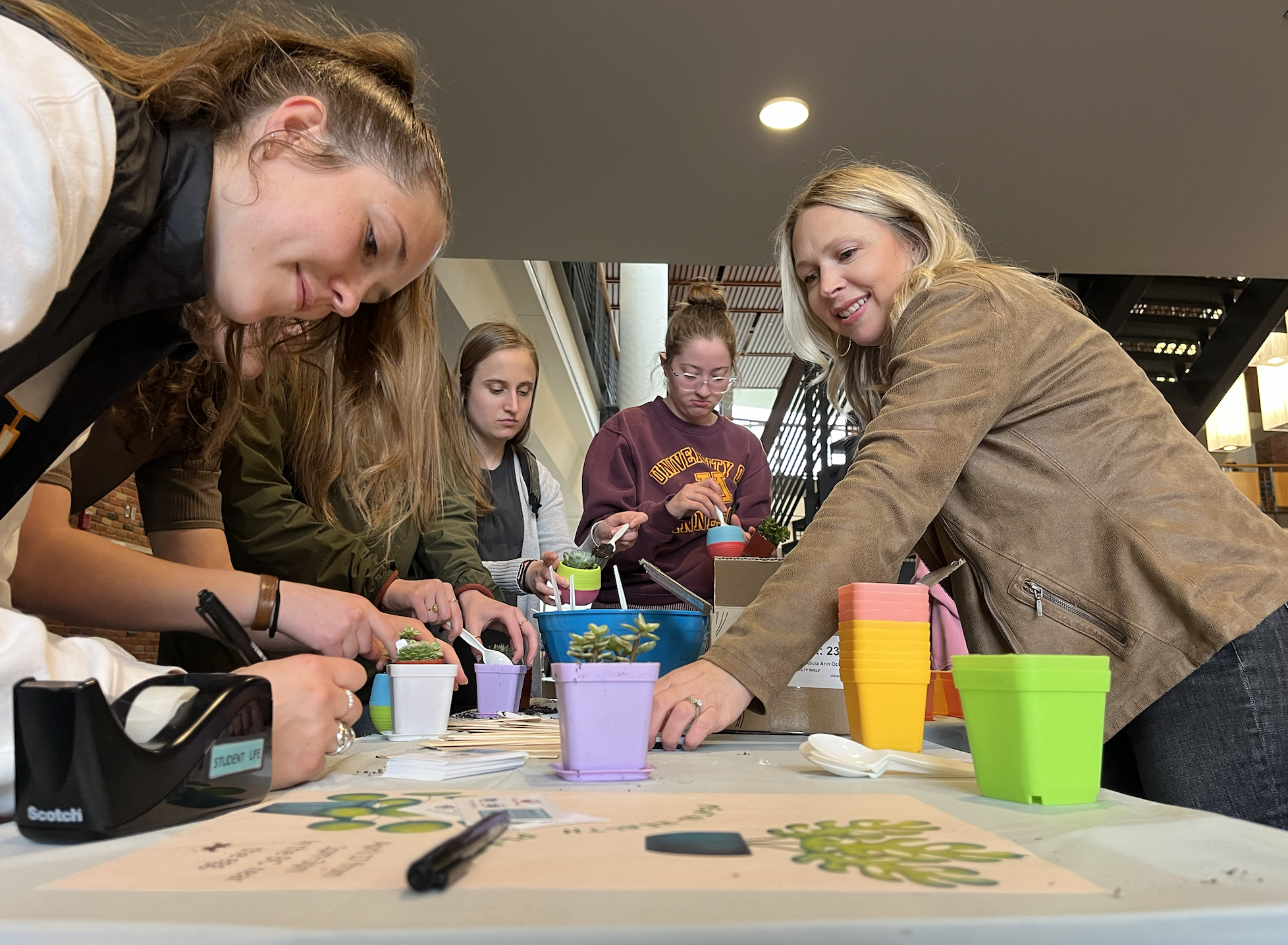 Bethel University senior Hailey Gregg leans in close to her plant as she writes its name down on one of the wooden sticks that have been provided, while Alisha Ochs, one of the organizers of the “get your emotional support plant” event smiles at her, passing more of the wooden sticks down to the end of the table. The event was held in the Brushaber Commons, Wednesday at 1:00 p.m. and was planned by Be Well at Bethel to raise awareness of the importance of mental health.