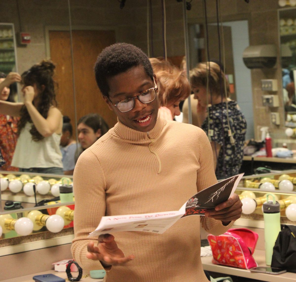 Nate Holder reads a program to his castmates in the dressing rooms before their first showing of “The Plot, Like Gravy, Thickens” April 18.  “I do get a little nervous performing in front of an audience,” Holder said. “But once I get into it … I can picture the room empty and just do my thing.”