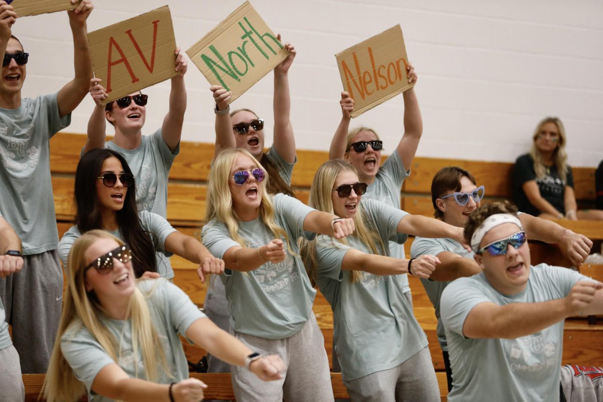 The commuter cheer team, wearing sunglasses and gray sweatpants, sings about the struggles of commuting and finding a parking spot during cheer night Oct. 13, 2025, in the Robertson Center gym at Bethel University.