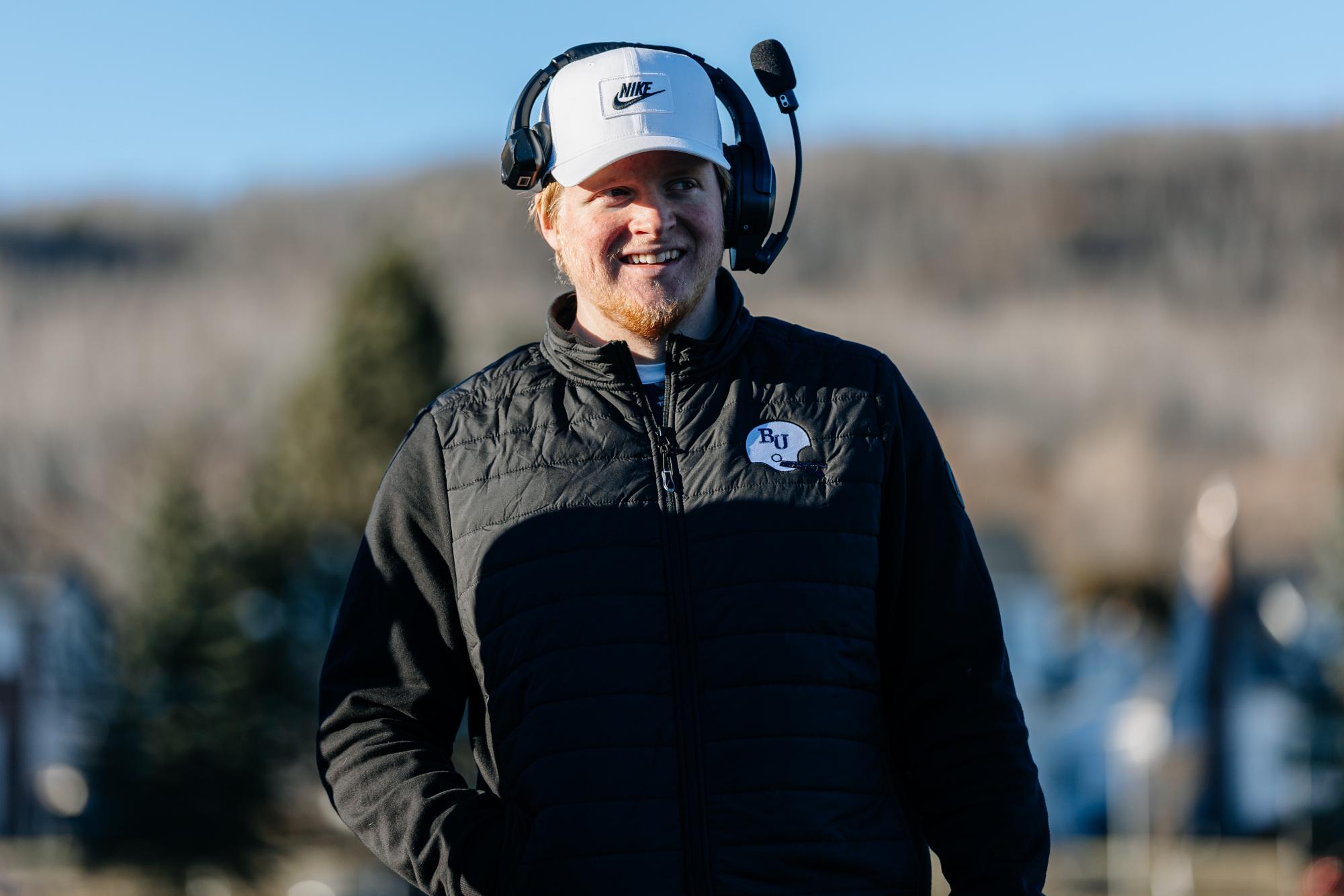 Senior student specialists coach Ben Frey smiles amidst the Bethel University Royals football team’s 62-0 win at the College of Saint Scholastica Saturday, Nov. 15. Frey entered his time at Bethel hoping to be the team’s starting kicker, but blood clot complications in the spring of 2025 sidelined him indefinitely. “Who knows what the actual meaning behind it was?” Frey said. “But now I'm starting to see it a little bit with the coaching.” 